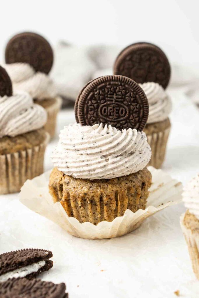 Several cupcakes with the wrapper pulled down a swirl of frosting and an Oreo cookie on top.