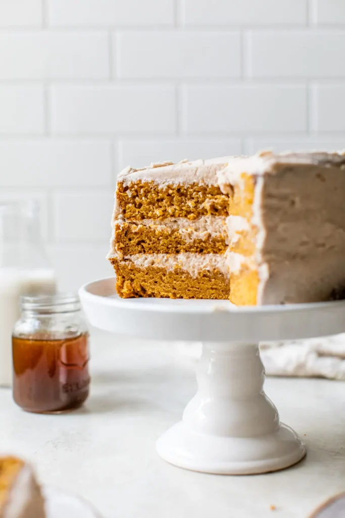 Three layer pumpkin cake with plenty of frosting on a white cake stand. 