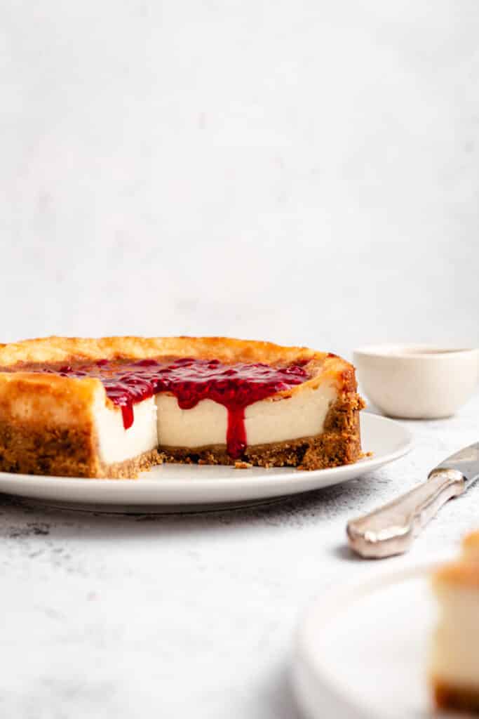 Vegan New York style cheesecake with a third cut out and topped with raspberry sauce.
