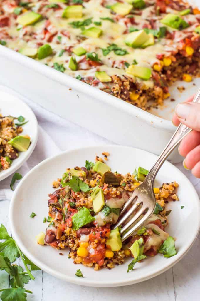 A person taking a fork from a plate of Mexican quinoa casserole, part of the collection "60 Vegan Casserole Recipes.