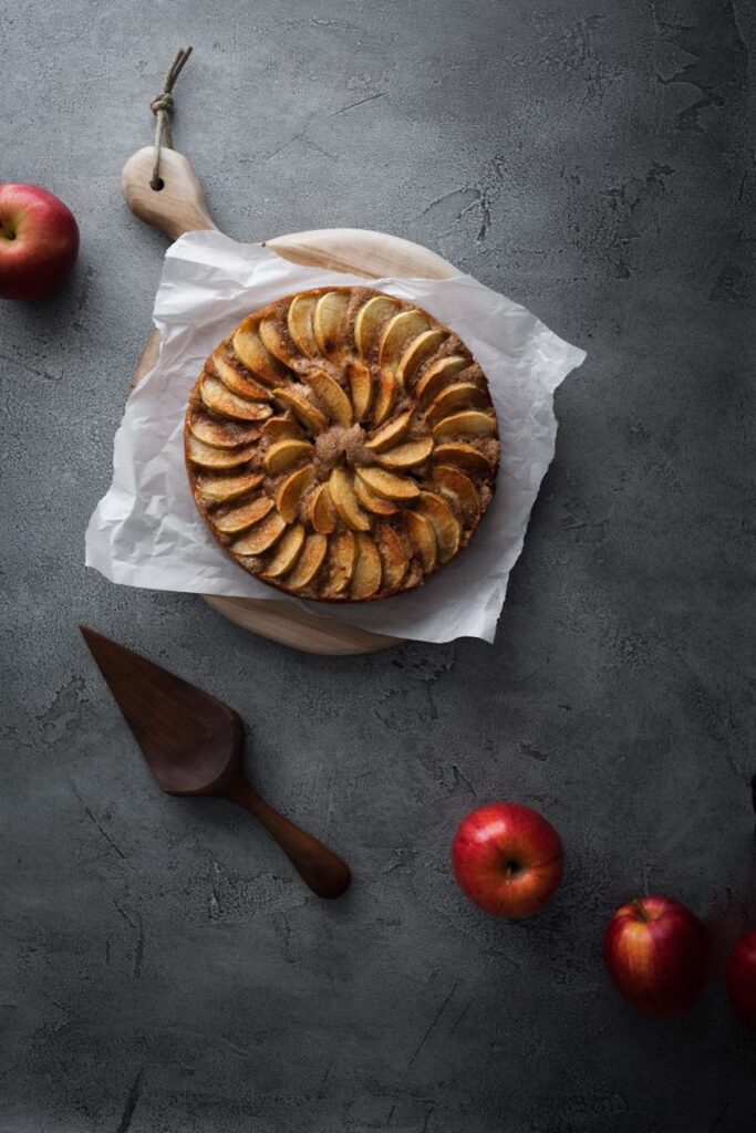 Stunning apple cake with sliced apples on top sitting on a gray surface.