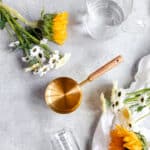 Sunflowers and daisies next to a golden measuring cup with a wooden handle.