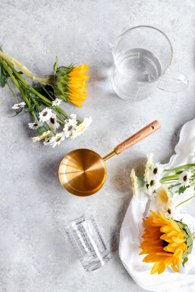 Sunflowers and daisies next to a golden measuring cup with a wooden handle.