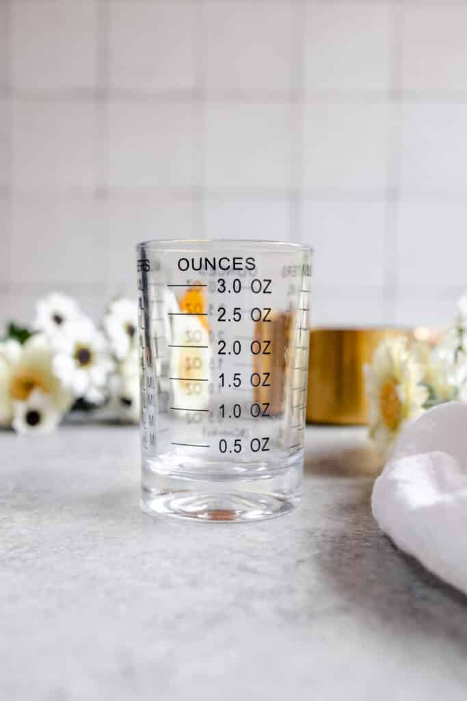 Three ounces measuring glass with flowers in the background.
