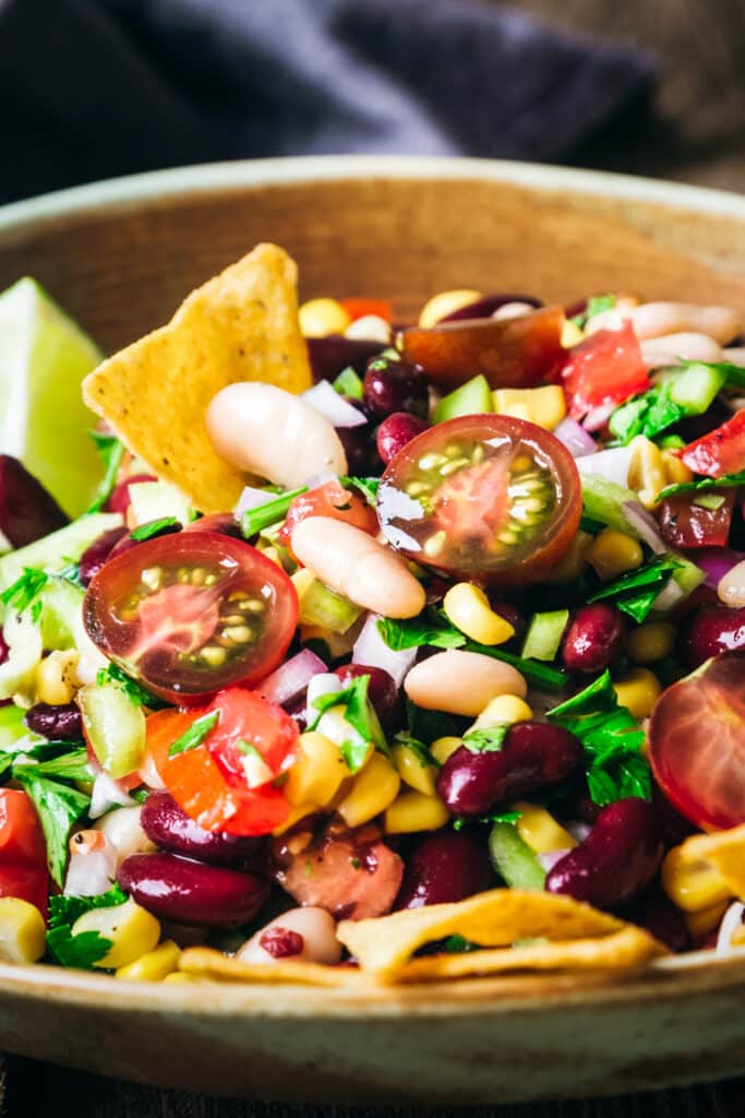 Tan and green shallow bowl with sliced cherry tomatoes, white beans, kidney beans, and more.