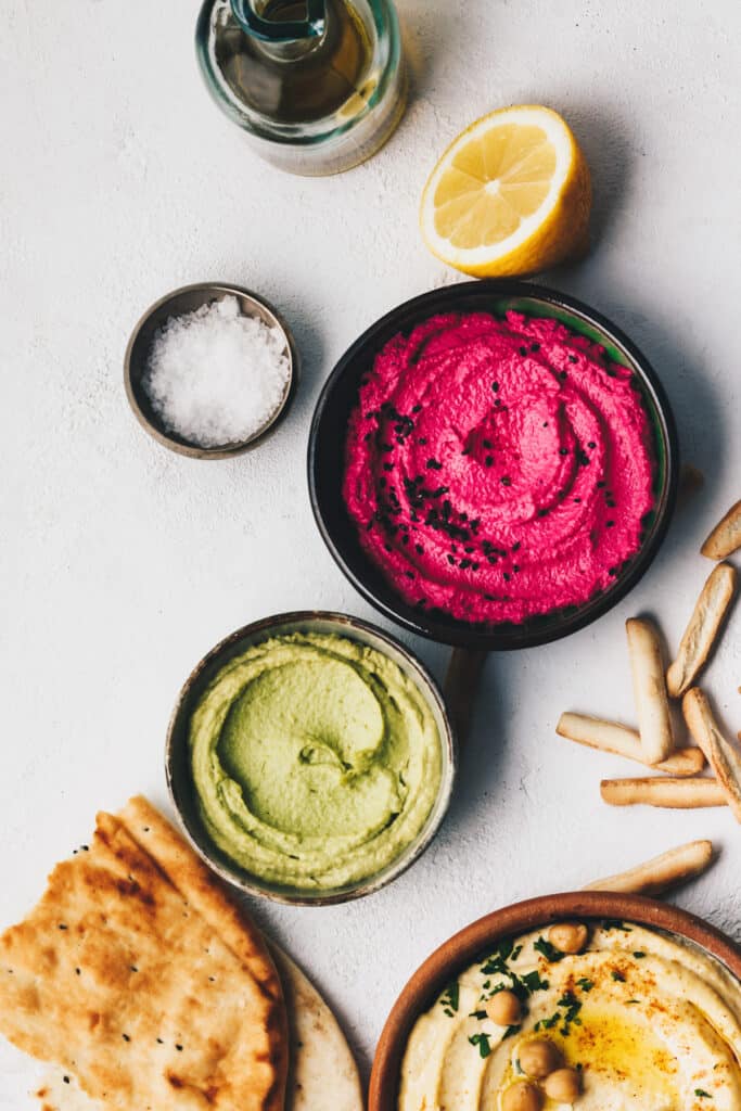 Vibrant beet root hummus with black sesame seeds on top, half of a lemon and flake salt next to it.