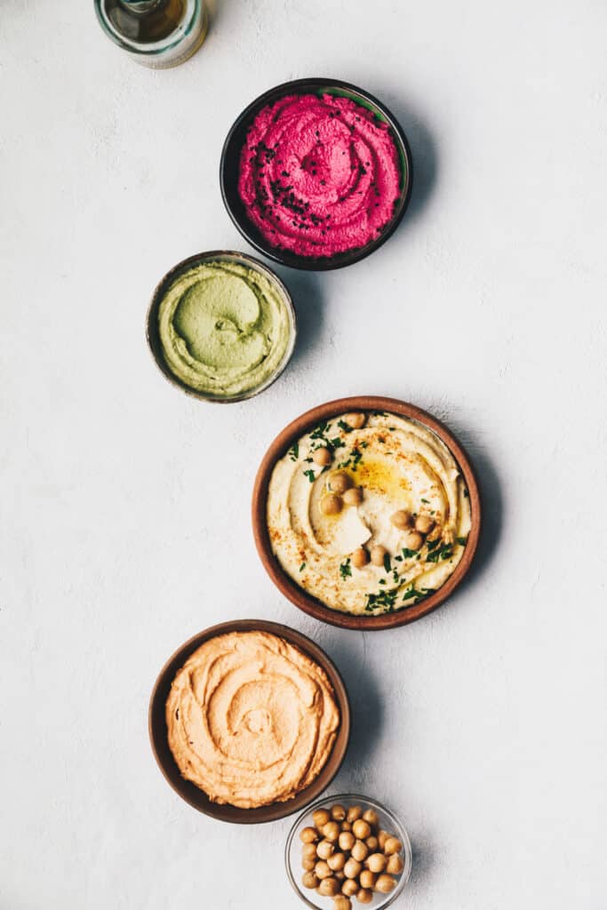Three different types of hummus on a light gray surface.