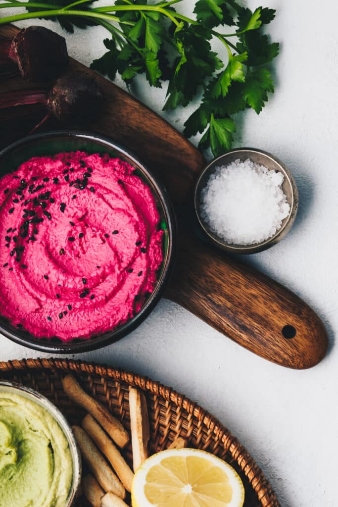 Bright pink beet hummus on a wooden board with fresh parsley.
