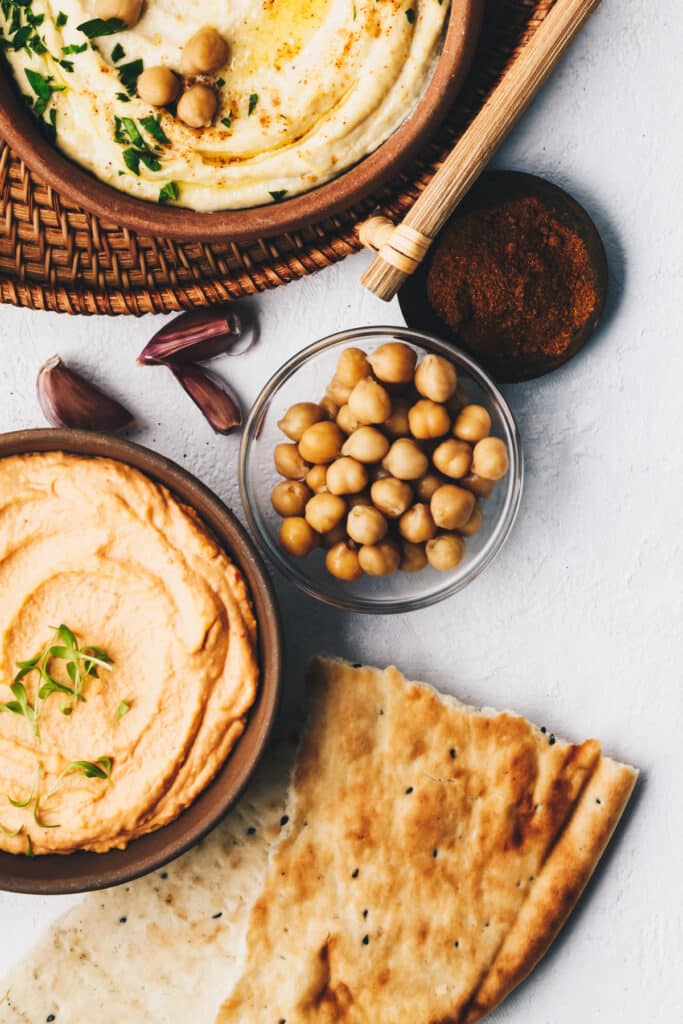 Small bowl of chickpeas with larger bowls of hummus surrounding it.