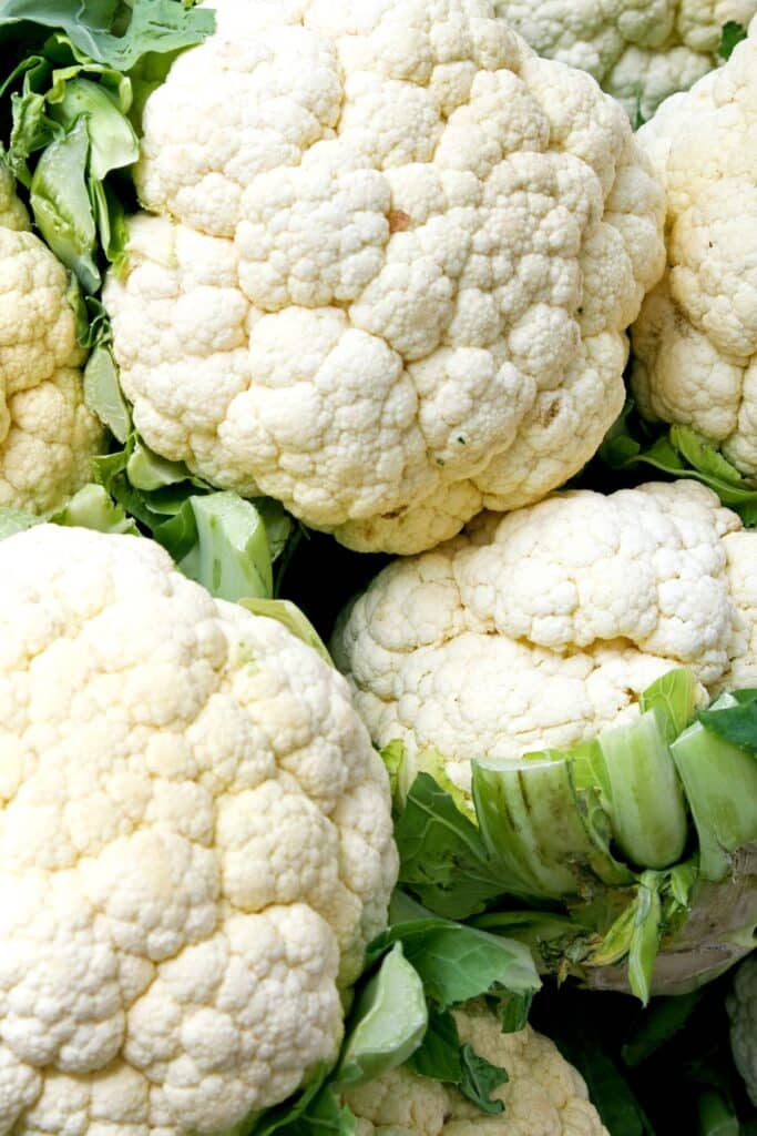 White cauliflowers with green leaves in a pile.