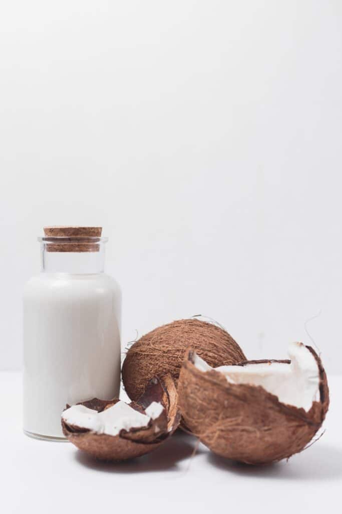 Glass container with cork lid filled with coconut milk with fresh coconuts next to it. 