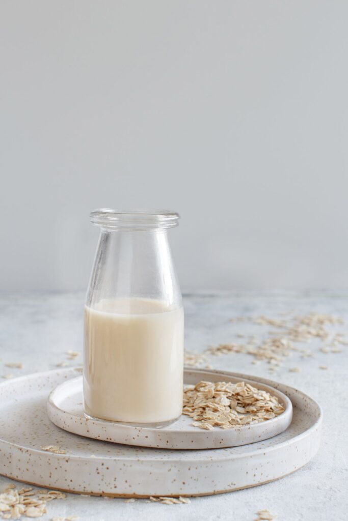 Glass pitcher of homemade oat milk on a white ceramic plate.