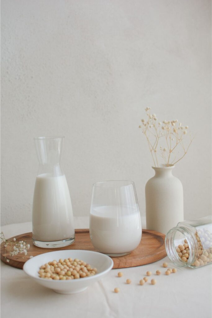 Homemade soy milk in glass jars and cup on a wooden cutting board. 