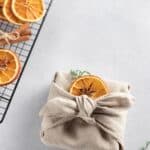 Christmas gift wrapped in linen fabric with dried oranges on top.