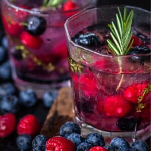 Two cups of blueberry and raspberry infused water with rosemary sticking out.