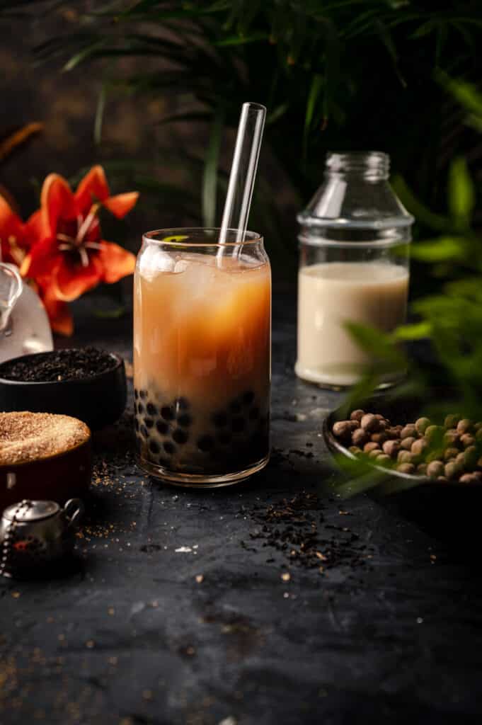 Black counter with ingredients for bubble tea and a glass of freshly made classic milk tea.