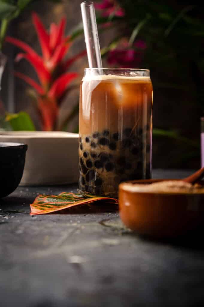 Glass of coffee bubble tea with a bowl of raw sugar in front of it.