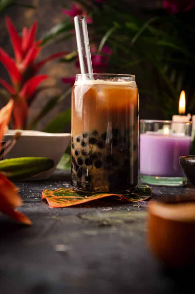 Coffee boba tea with tropical plants behind it.