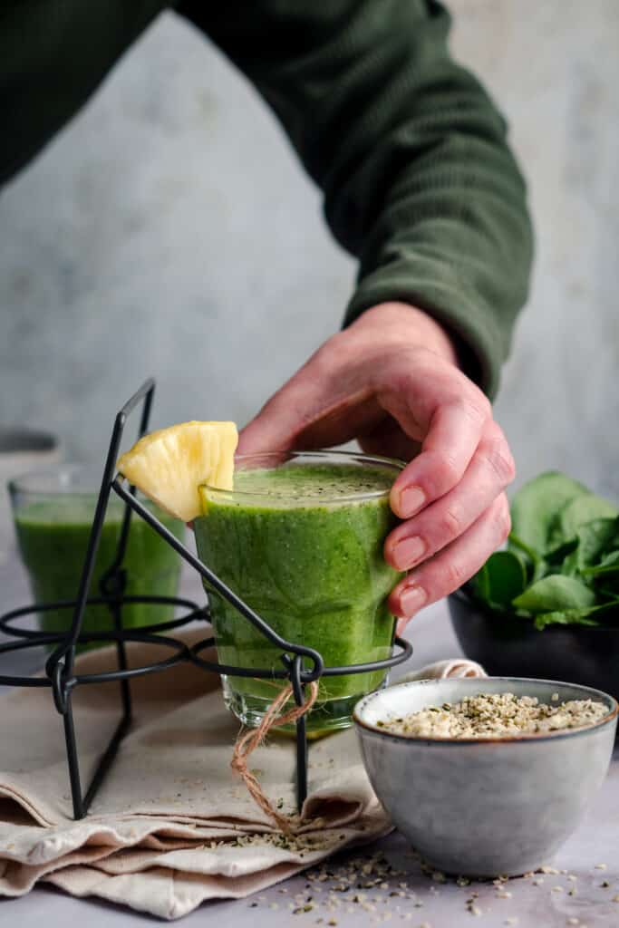 Woman reaching for a cup of pineapple spinach smoothie with a bowl of hemp hearts next to it.