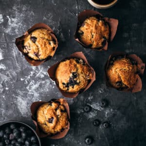Banana blueberry muffins that were baked sitting on a charcoal colored surface.