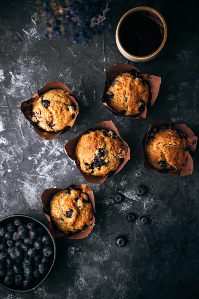 Banana blueberry muffins that were baked sitting on a charcoal colored surface.