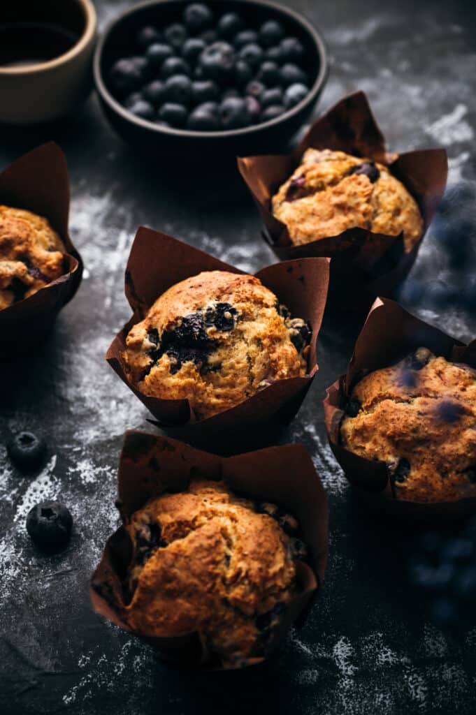 Several vegan muffins with a bowl of blueberries in the background.