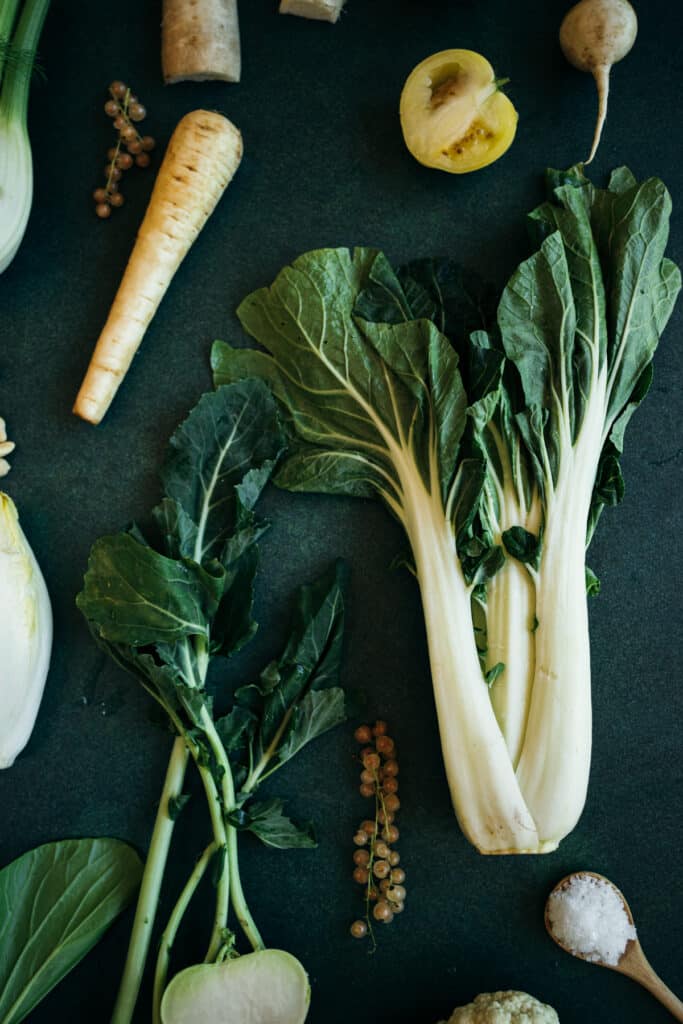 Giant bok choy with dark green leaves, white tomato sliced in half, and parsnips.