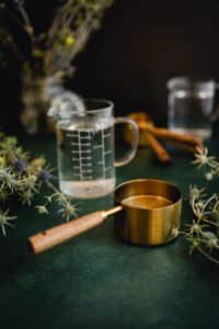 Gold and wooden measuring cup with a glass liter measuring cup behind it.
