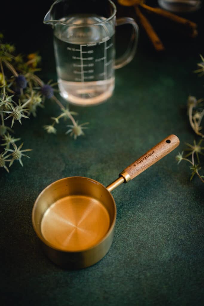 Gold and wood measuring cup  with flowers around it on a green counter.