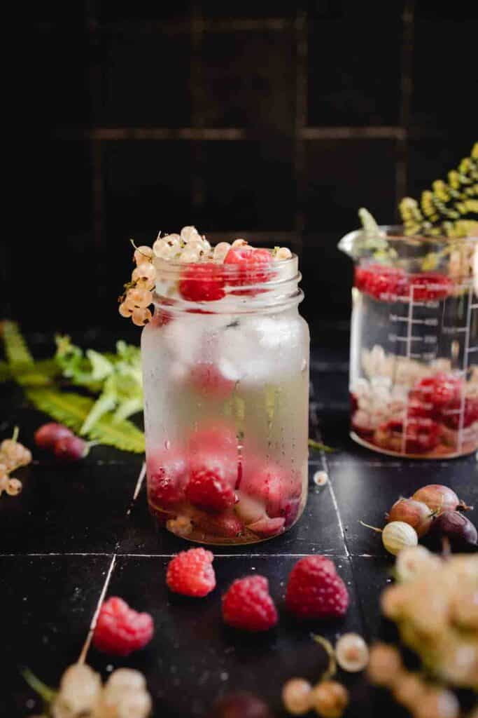 Infused berry water in a pint jar on a black tiled counter.
