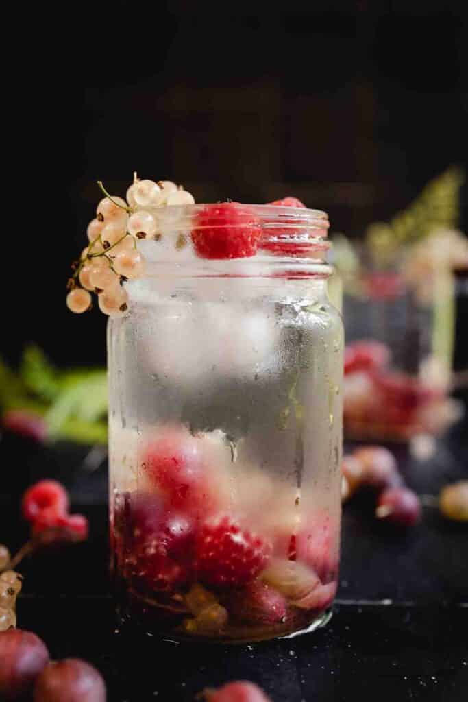 Close up of pint jar filled with berry water and white currant berries overflowing from the top.