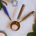 Close up of gold and wood measuring cup and tablespoon with a purple-blue flower next to it.