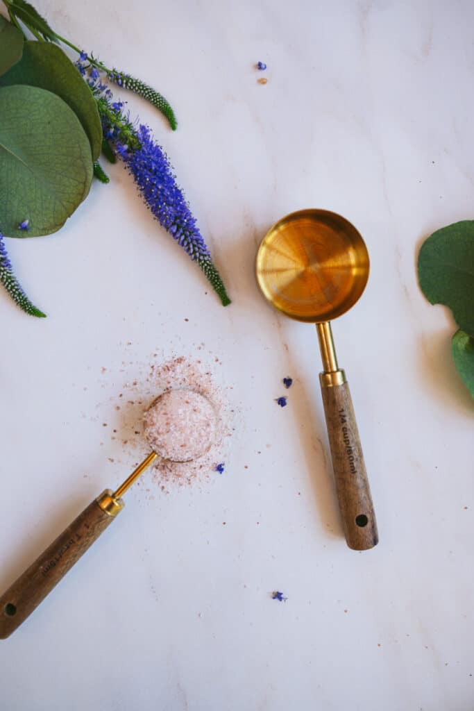 Gold and wood meauring utensils with the tablespoon overflowing with pink salt.