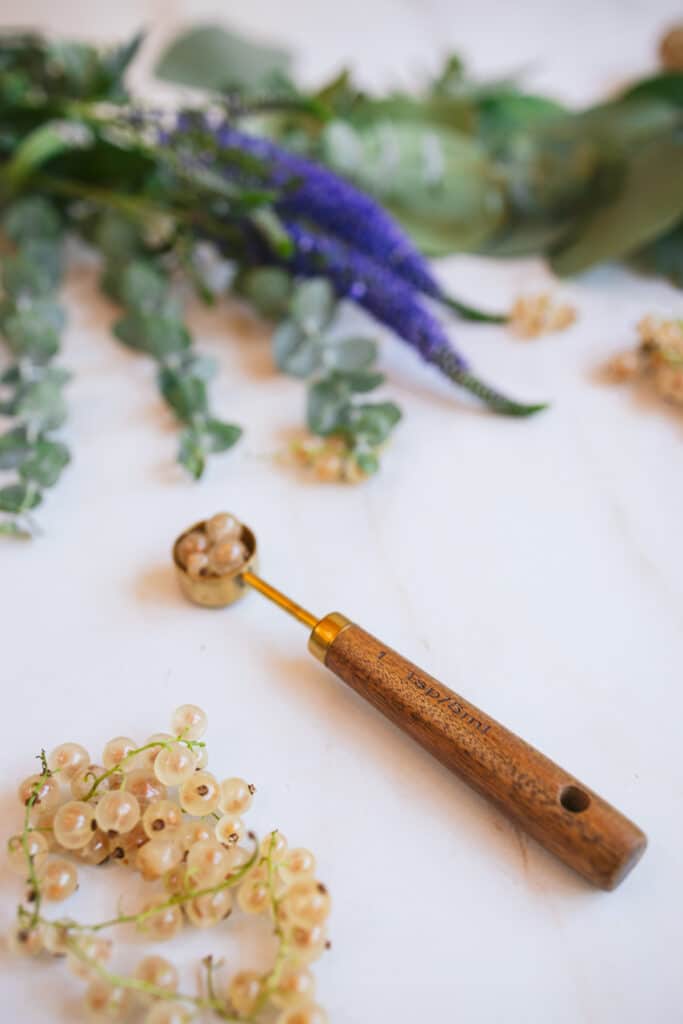White currant berries next to a wooden handled teaspoon on a marble counter.