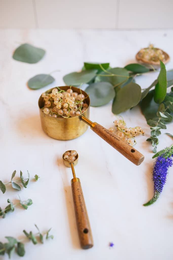 Angle photo of brass and wood measuring utensils on a marble counter with purple flowers and eucalyptus.