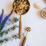 Gold and wood measuring cup and teaspoon filled with white currant berries.