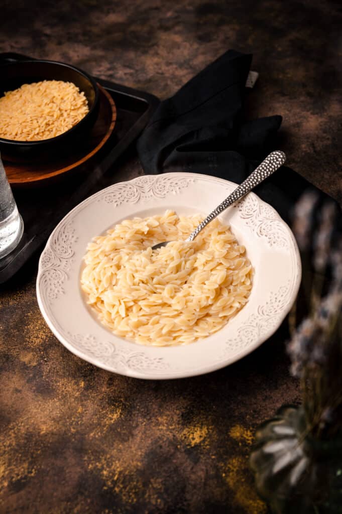 Bowl of cooked orzo with a metal spoon sticking out.