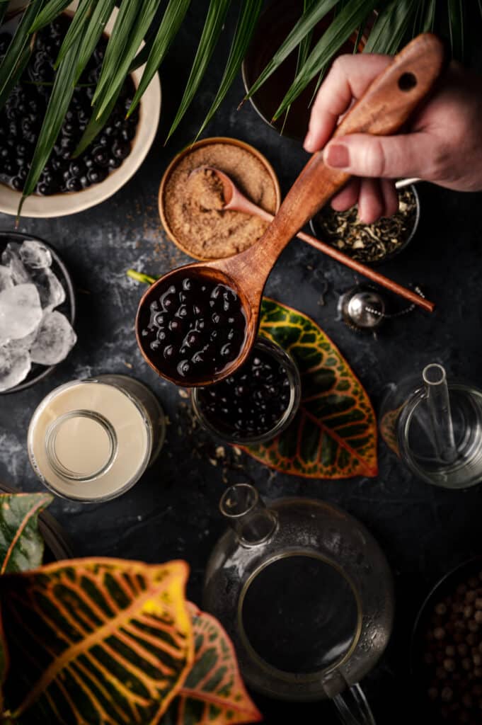 A hand is pouring black berries into a wooden spoon.