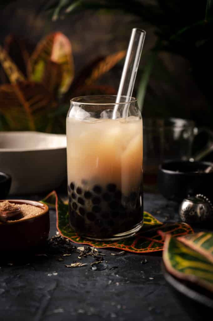 Jasmine milk tea in a clear glass cup sitting on top of a tropical leaf.