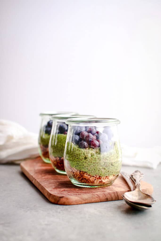 Three jars of matcha chia pudding lined up at an angle down a wooden board.
