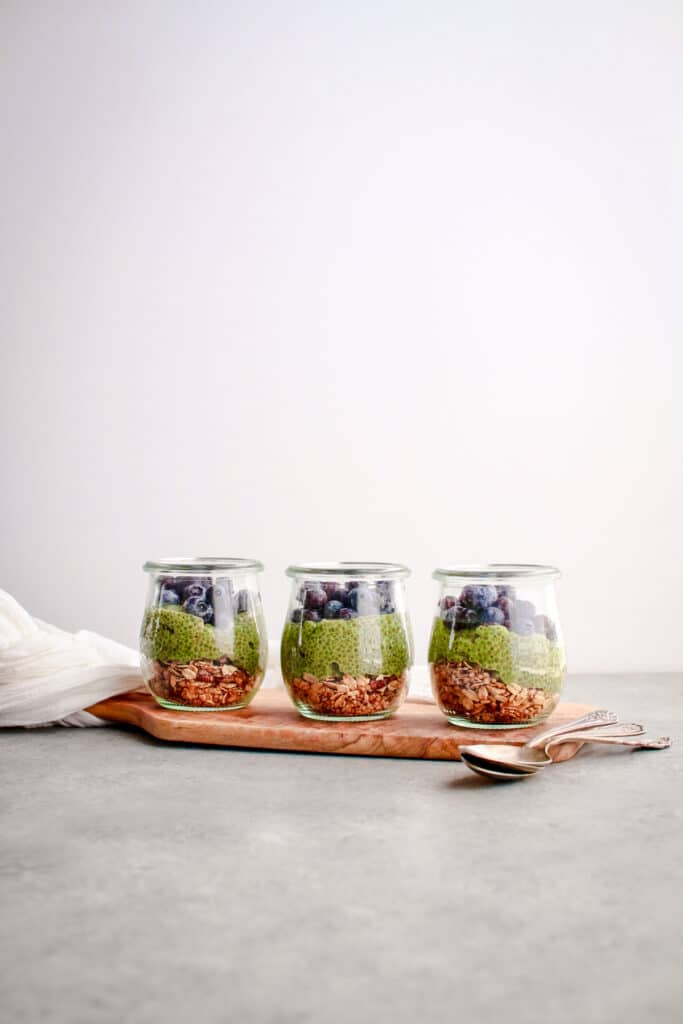 Three tulip glass jar filled with matcha chia pudding on a wooden board.