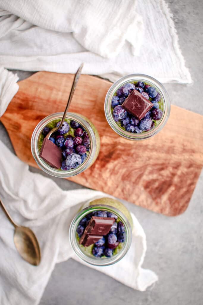 Three jars of chia pudding topped with blueberries and a chocolate square.