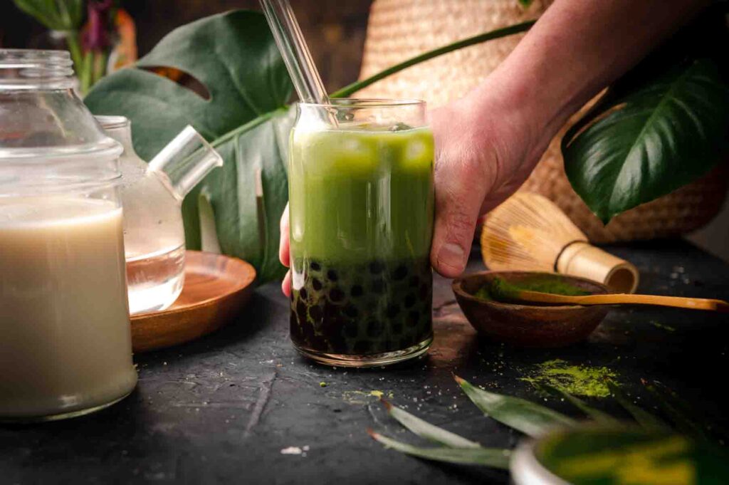 Woman reach for a glass of matcha milk tea with ingredients surrounding the cup.