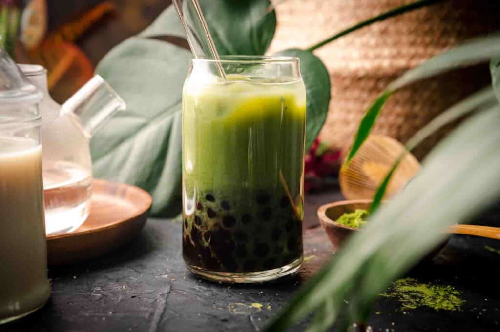 Image of tropical plant leaves with a glass of green matcha boba tea.