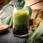 Image of tropical plant leaves with a glass of green matcha boba tea.