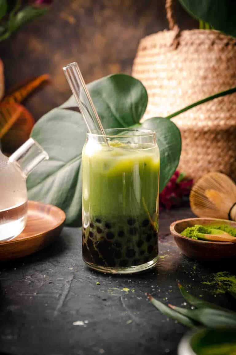 Matcha milk tea with boba in a clear glass with bubble tea straw.