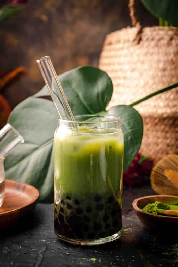 Matcha milk tea with bubbles in a Libby glass with monsterra leaves behind it.
