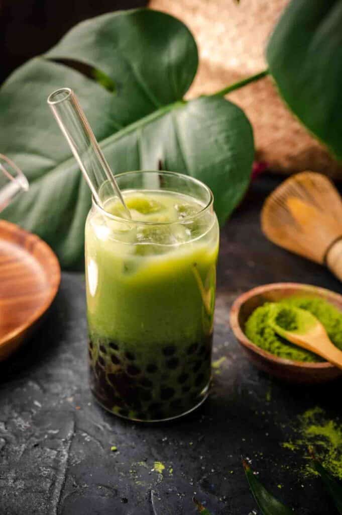 Tapioca pearls at the bottom of a glass filled with matcha milk tea.