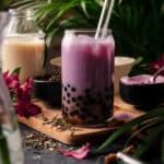 Purple taro milk tea with flowers and tropical plants behind it.