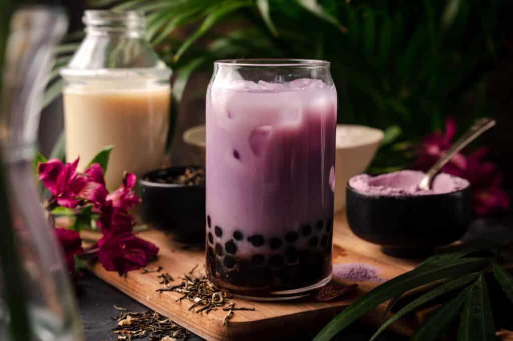 Taro milk tea and ice added to the clear glass cup with tapioca balls.